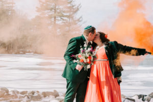 couple posing for wedding photos with smoke bombs at frozen lake