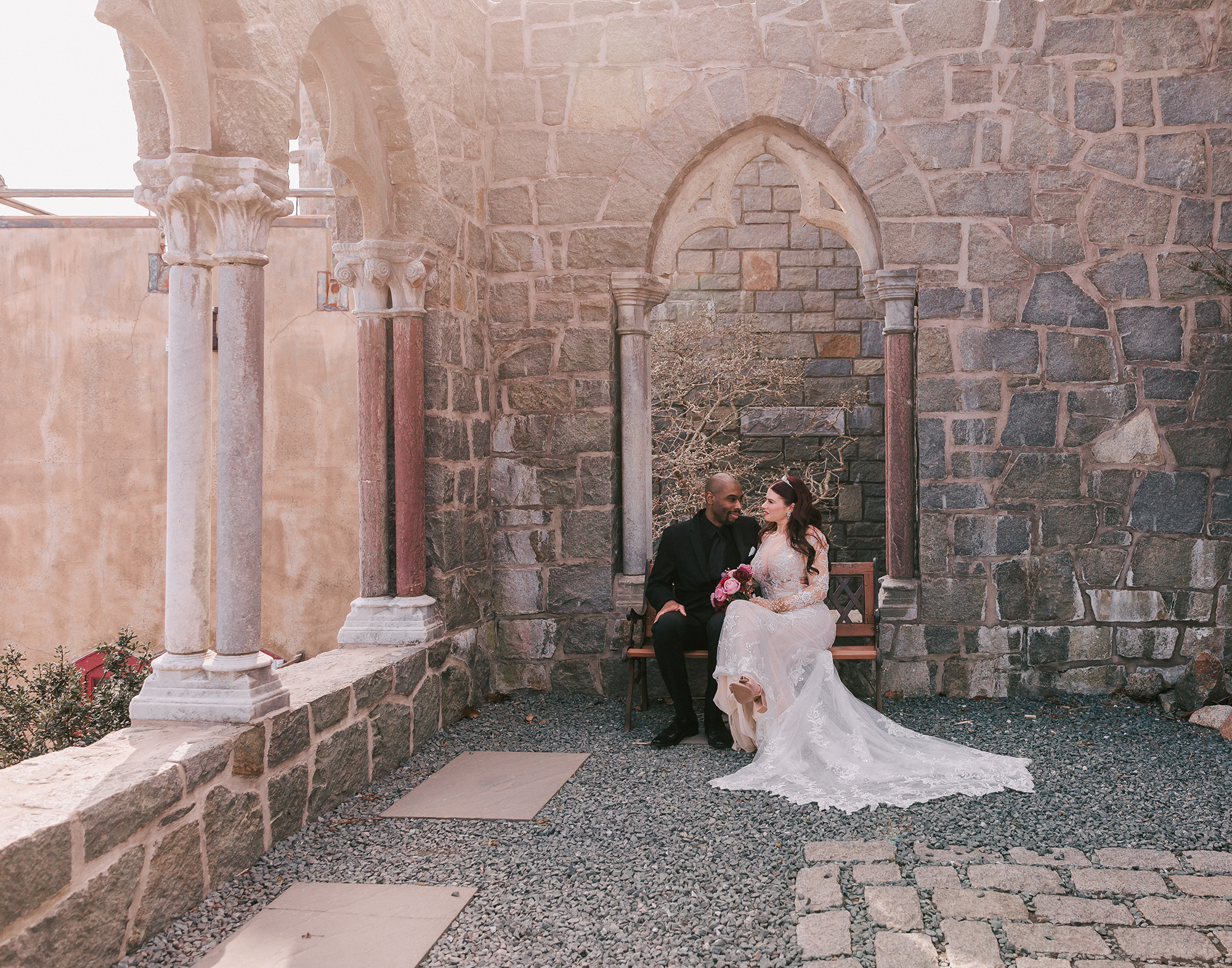 newlywed couple sitting on a bench outside Hammond Castle, an enchanting wedding venue on the North Shore of MA
