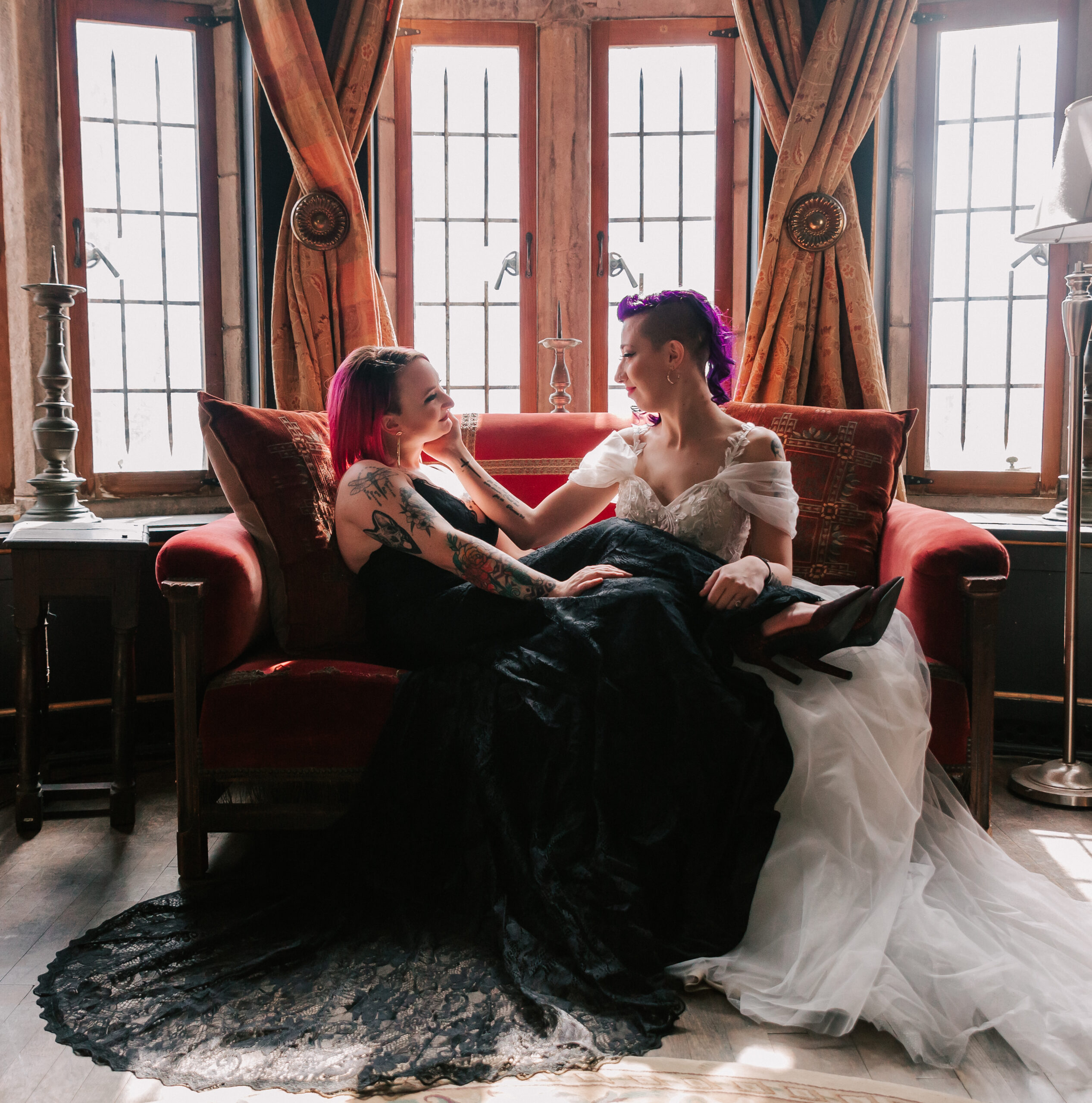 two brides, one in a white dress and one in a black dress, sitting in the library of Hammond Castle on their wedding day