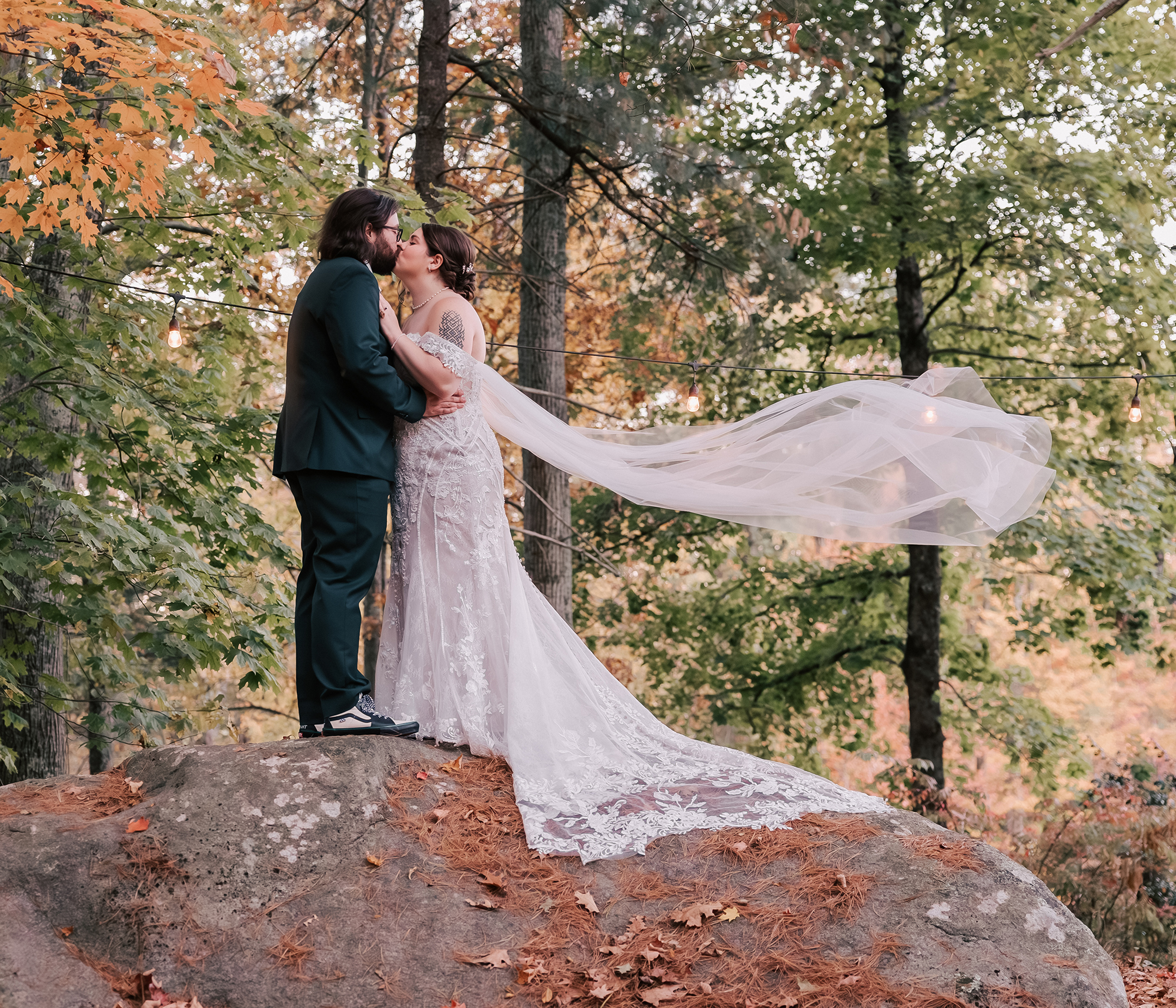 bride and groom kissing on rock in woods outside wedding venue in Hopkinton, MA