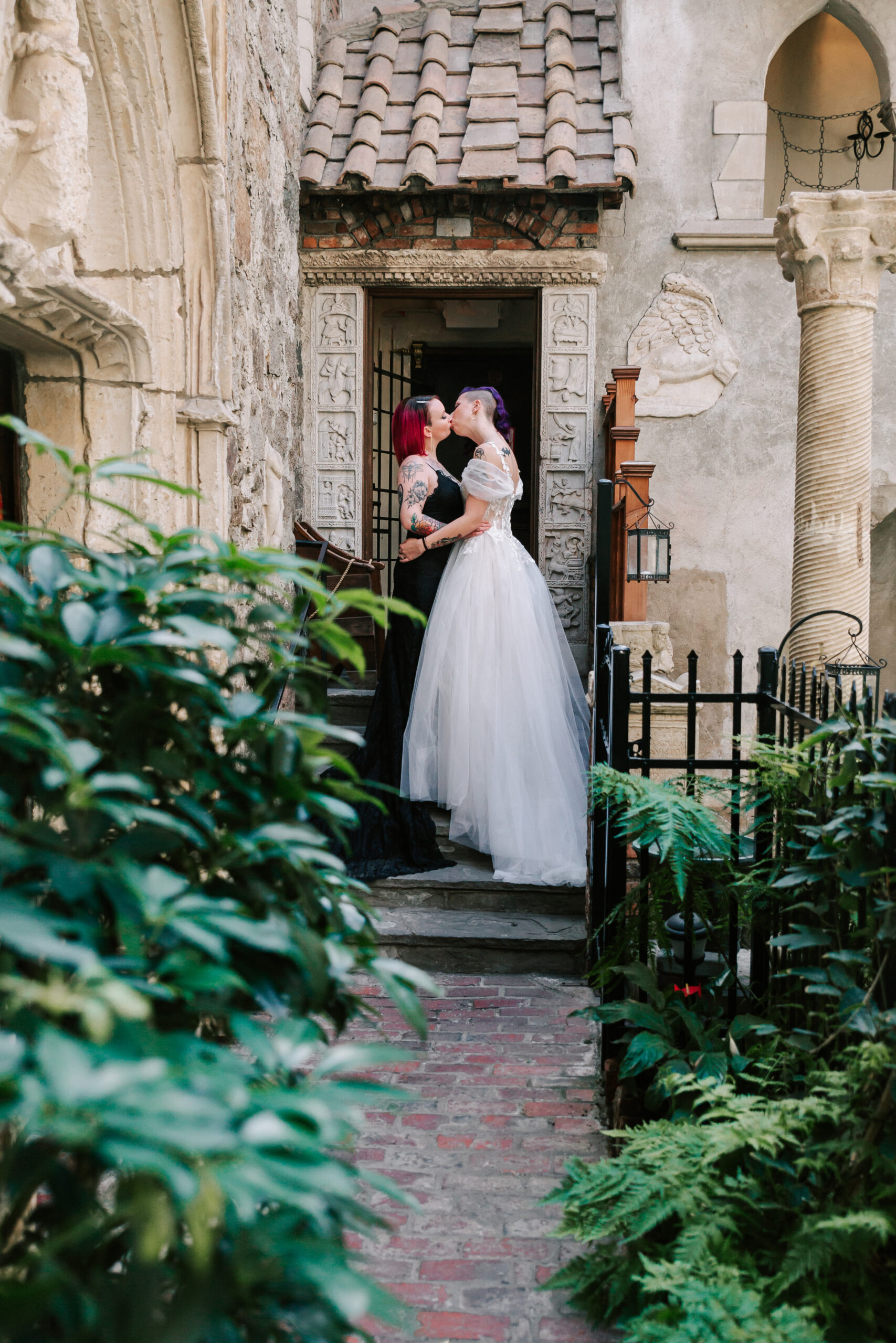 two brides kissing on steps in greenhouse of Hammond Castle, a unique North Shore MA wedding venue